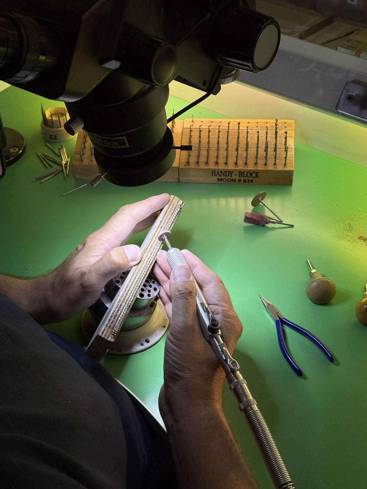 Sertisseur au travail sous loupe binoculaire, fraises et outils suspendus — atelier SKJ Serti, Anvers